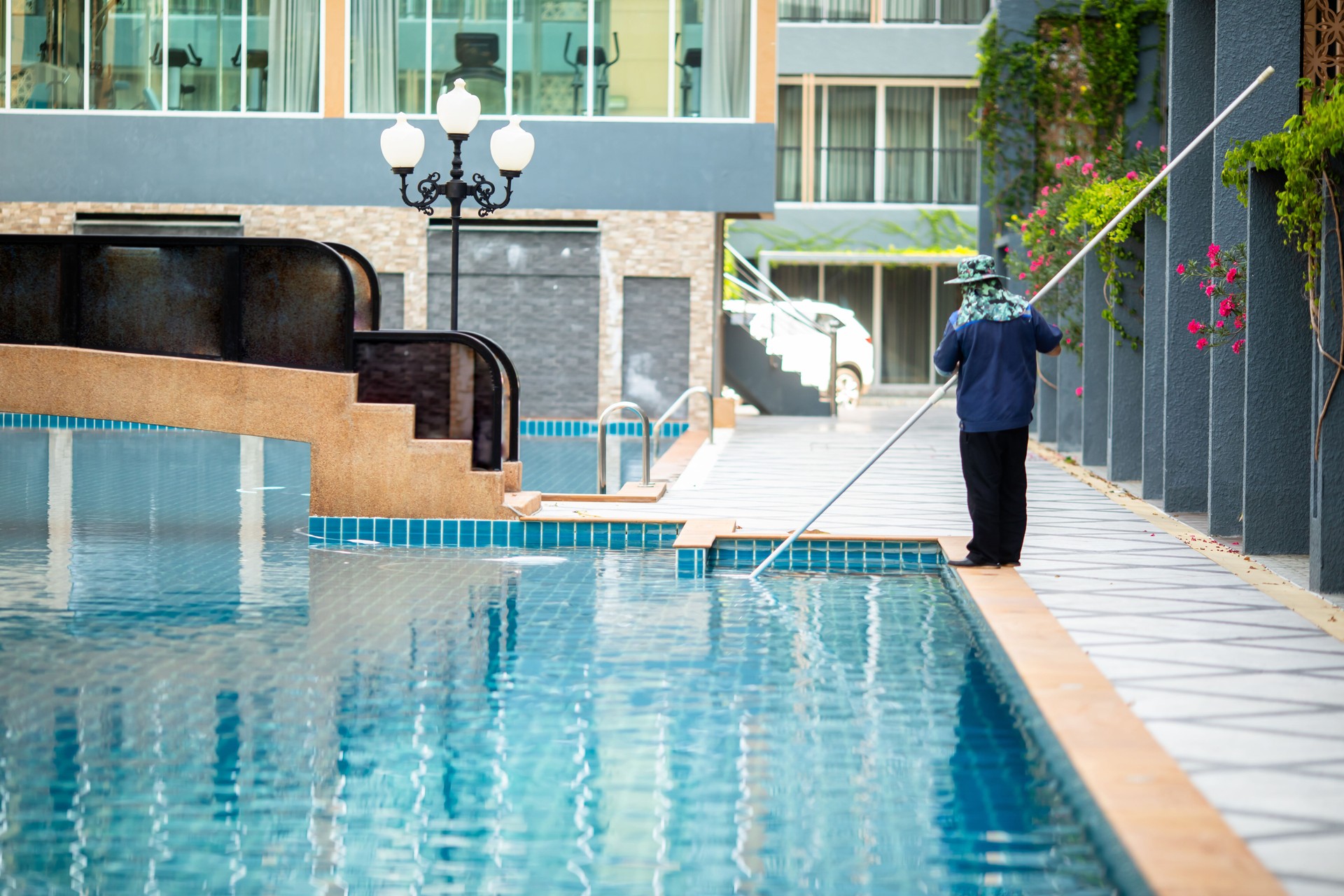 Staff are cleaning the hotel pool using an underwater vacuum pump.